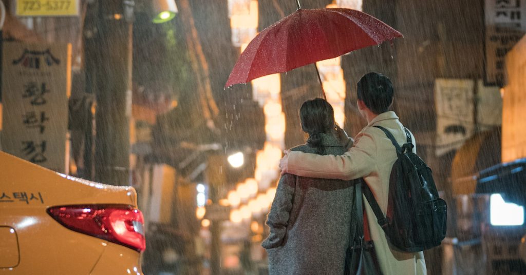 Casal de Something in the Rain com guarda-chuva vermelho.